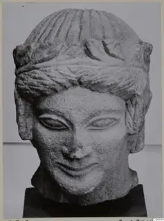 Carved limestone head with a bust-like neck and banded hair, shown on a black stand from Mersinaki