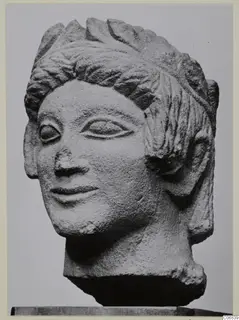 Limestone head from Mersinaki with layered hair and a faint smile, photographed against a plain grey background
