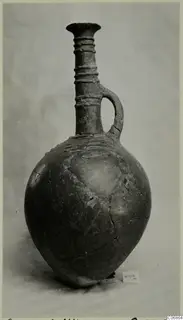 Pottery jug with a tall ringed neck, single loop handle and rounded body, photographed against a plain grey background.