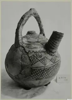 Jug with a strap handle, a side spout and painted geometric bands in dark paint on a pale ground