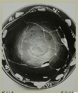 Interior of a broken dark bowl with white painted rim decoration and a stamped rosette at the centre