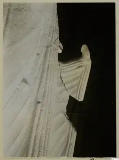 Close view of a white limestone sculpture fragment from Vouni, with carved parallel folds, photographed against black.