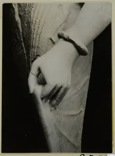 Sculpted hand and wrist of a limestone statue, with a thick bangle, fingers curled over a fold of drapery