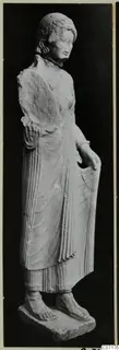 Limestone statue of a standing woman with a curled headdress, from Vouni, shown against a black background