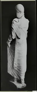 Back view of a limestone statue of a standing woman from Vouni, against a dark background