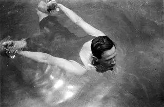 Man swimming face-down in clear sea water, seen from above with arms outstretched.
