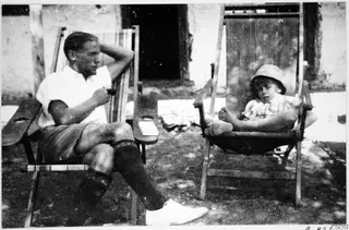 A man and a child relaxing in wooden deck chairs in front of a whitewashed wall at Machairas.