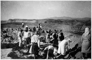 Workers at an excavation among stone remains, with hills and mountains in the distance