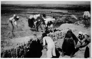 Workers digging a trench at an excavation, with flat land and low hills in the distance