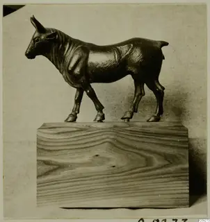 Small bronze figure of a four-legged animal with short upright horns, standing on a wooden block.