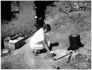 Woman crouching beside a bowl, apparently washing, at Machairas