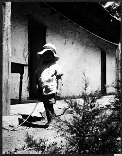 Stefan Gjerstad, a small child in a sun hat, standing outside a plastered building at Machairas
