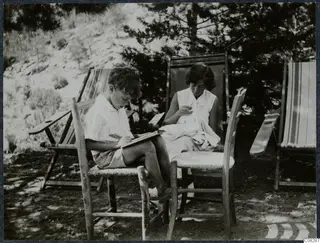 Martin Gjerstad and Vivi Gjerstad outdoors at Machairas, one writing in a notebook, one sewing, among deck chairs