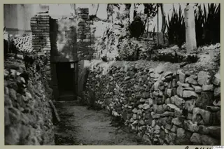 Narrow path between dry-stone walls leading to a doorway in a stone wall