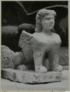 Stone sculpture of a winged creature with a human face and curly hair, standing on a rectangular base, from Soli