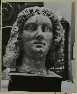 Carved head and bust with curled hair pierced by drilled holes, on a dark rectangular base