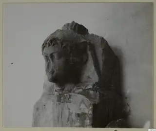 Carved stone head and upper body of a statue, broken at the top and right shoulder, on a rectangular base