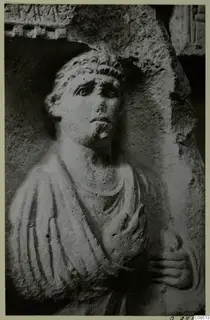 Carved stone figure of a man with curly hair and a short beard, one hand raised to his chest, in North Africa