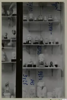 Glass display case holding heads, busts and statues on shelves, with blue handwritten numbers on the glass