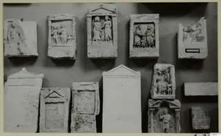 Carved stone slabs and reliefs fixed to a wall in two rows, with standing and seated figures