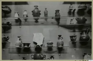 Small jugs, juglets and bowls arranged on wall-mounted shelves in a display case
