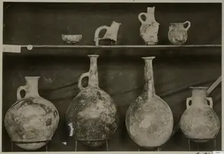 Jugs and a bowl from Lapithos Markides, T.5, set out on two shelves against a dark drape