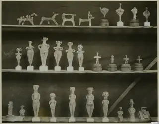 Three shelves of terracotta figurines: small animal figures, standing human figures and stylised idols on bases.