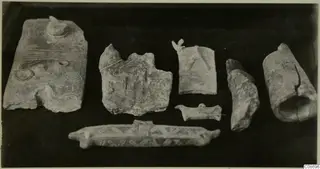 Seven pale objects on a dark ground: an incised rectangular piece, tubes, a small bird-like piece and a long bar with a chevron pattern.