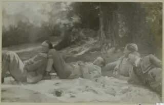Four men lying and reclining on a blanket under trees, one with a pipe.
