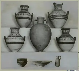 Group of nine pottery vessels from Marion Tomb 71: four painted handled jars, a plain jar and small bowls and a juglet, arranged on a shelf