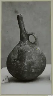 Pottery vessel with a rounded body, long narrow neck and loop handle, photographed on a pale surface