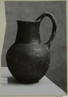 Dark-surfaced jug with a single loop handle, photographed on a pale surface