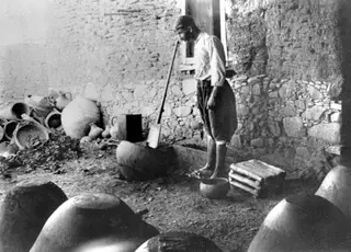 Potter treading clay in a courtyard at Klirou, with large jars and pots around him