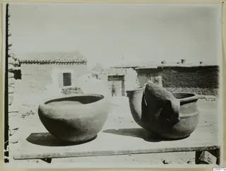 Two new clay pots on a wooden table in a courtyard at Klirou, with houses behind.
