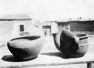 Two large clay pots on a wooden table in a courtyard of tiled, mud-brick buildings at Klirou