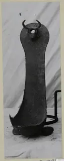 Corroded metal object with a long flat handle, a knob with two curved projections at the top and a shallow bowl-shaped end.