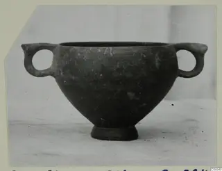 Dark grey two-handled bowl with a short foot, photographed on a light surface against a pale backdrop.