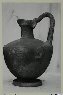 Pottery jug with a single loop handle and ring foot, photographed on a plain backdrop