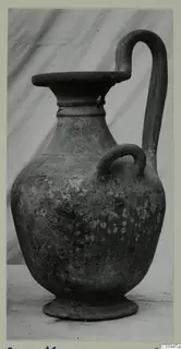 Pottery jug with a tall strap handle, a small loop handle on the body and a wide flat-topped mouth