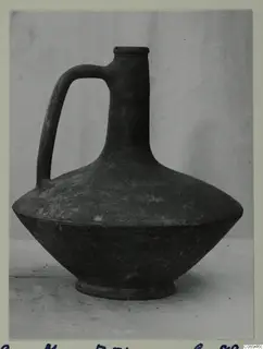 Single-handled pottery jug with a narrow neck, flat rim and wide, sloping body, shown on a plain backdrop