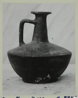 One-handled dark jug with a flared rim, narrow neck and ring base, shown against a grey backdrop.
