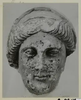 Stone statue head from Arsos, with wavy hair in layered bands and a pitted, chipped surface.