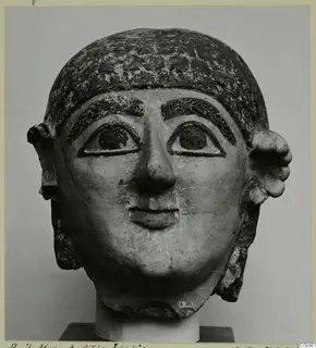 Terracotta head with a painted hairstyle, large ears and a calm face, shown on a stand.