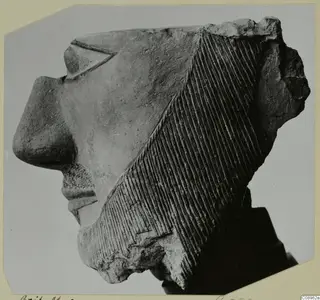 Broken terracotta head in profile facing left, with diagonal incised lines across the hair at the back