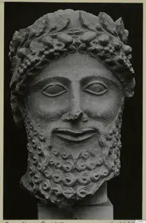 Limestone head of a bearded male figure with a wreath of leaves and berries, shown against a dark background.