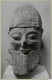Carved limestone head with a tall headdress and long beard, on a white pedestal, from Kition