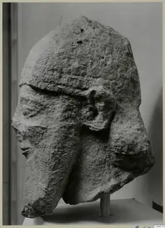 Weathered limestone head from Kition, shown in side view on a white pedestal
