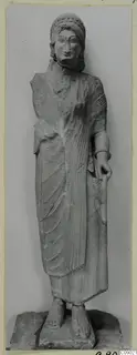 Limestone statue of a standing figure with a curled headdress, holding a tall rod, from Vouni.