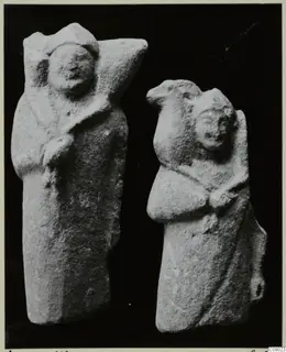Two limestone figurines of standing figures in draped garments, photographed against a black background