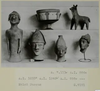 Statues, a footed bowl and an animal figure on a pale cloth, photographed as a print on a card mount.